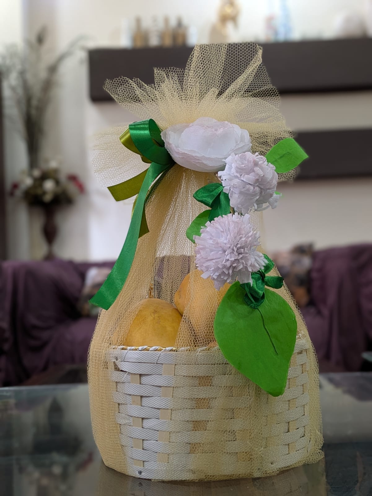 Hand holding a ripe yellow mango in front of a decorated gift basket